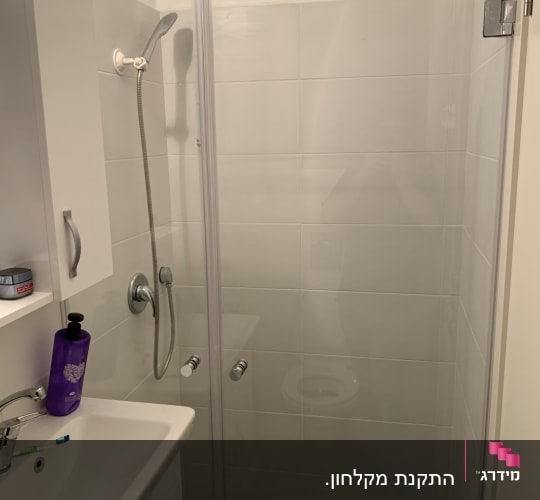 מקלחת עם דלת זכוכית וראש מקלחת כסוף